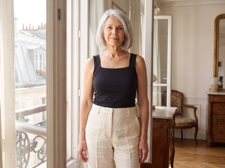 Femme d’une soixantaine d’années en débardeur Frinta noir près d’une fenêtre, à Paris